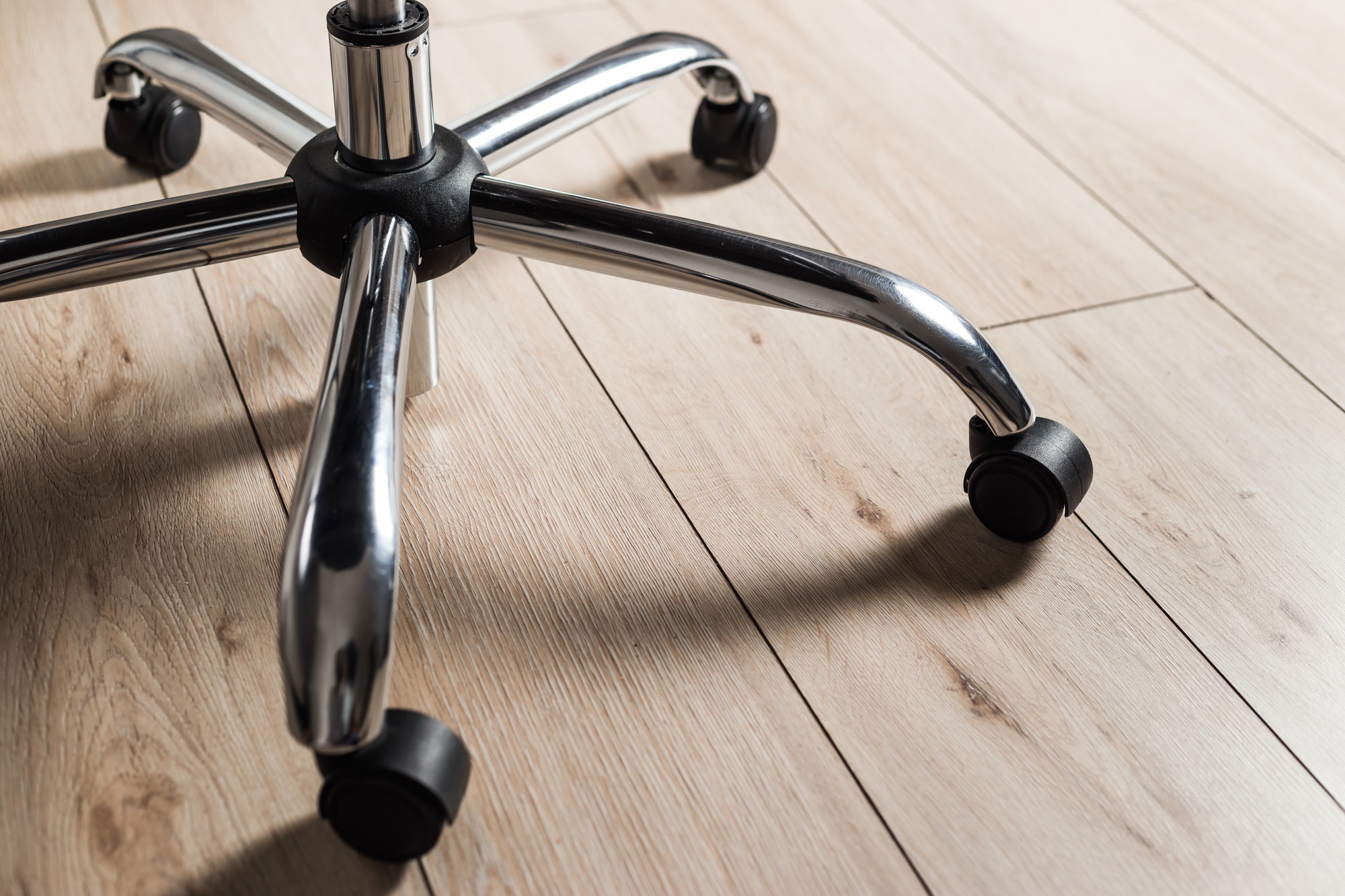Metal base of office chair with wheels on wooden floor, closeup